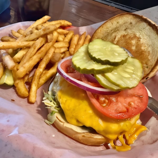 A Smitty's Bar cheeseburger with lettuce, tomato, onion, pickles, and a side of fries.